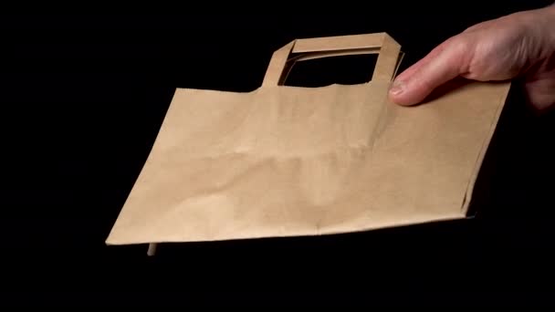 La mano masculina da un paquete de papel sobre un fondo negro. De cerca. Entrega para llevar y concepto de compras - Metraje, vídeo