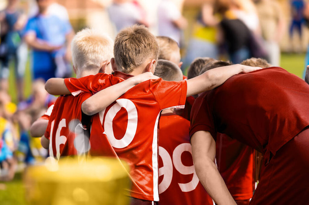 Діти в спортивній команді. Діти з молодшим футбольним тренером кружляють по колу. Команда хлопчиків у червоних сорочках збирається разом, щоб стратегічно, мотивувати або святкувати. Футбольні хлопчики досягли успіху в турнірі
 - Фото, зображення