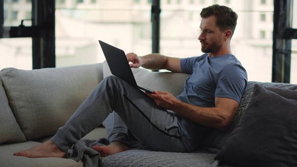 Człowiek z brodą pracujący zdalnie w domu. mężczyzna osoba siedzi na kanapie z komputer. - Zdjęcie, obraz