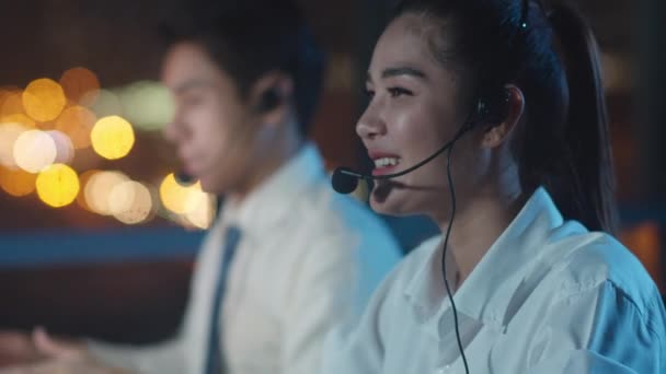 Millennial Asia young call center team or customer support service executive using computer and microphone headset working technical support in late night office. Concepto de trabajo de telemarketing o ventas. - Imágenes, Vídeo