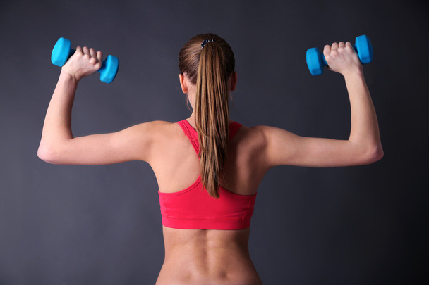Young beautiful fitness girl exercising with dumbbells, close-up, on gray background - Photo, image