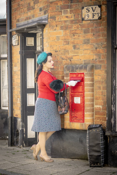Hermosa joven posando en ropa vintage de la década de 1940, publicando una carta en una esquina de la calle - Foto, Imagen