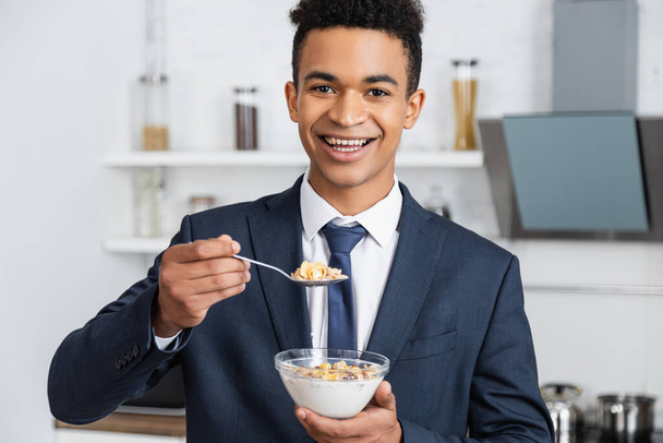 glücklich afrikanisch-amerikanischer Geschäftsmann hält Schüssel mit Cornflakes und Löffel  - Foto, Bild