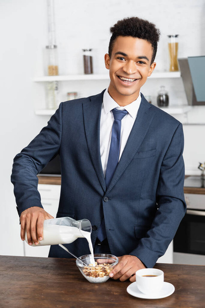 щасливий афроамериканський бізнесмен поливає свіже молоко в мисці з кукурудзяними пластівцями
  - Фото, зображення