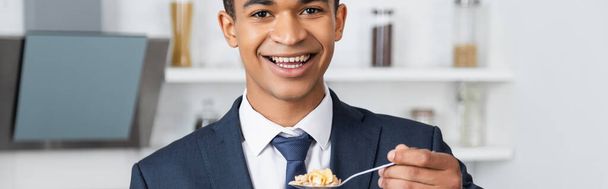 allegro uomo d'affari afroamericano che tiene cucchiaio con fiocchi di mais, striscione - Foto, immagini
