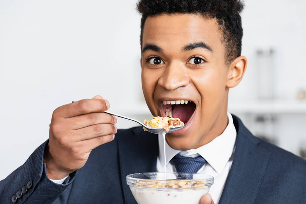 sorprendido hombre de negocios afroamericano comiendo hojuelas de maíz con leche  - Foto, imagen