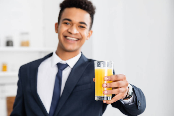 glass of orange juice in hand of happy african american businessman on blurred background  - Foto, afbeelding