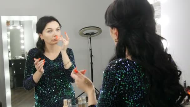 Joven hermosa mujer vistosa delante de un espejo aplica maquillaje y fundación o corrector con sus manos - Imágenes, Vídeo