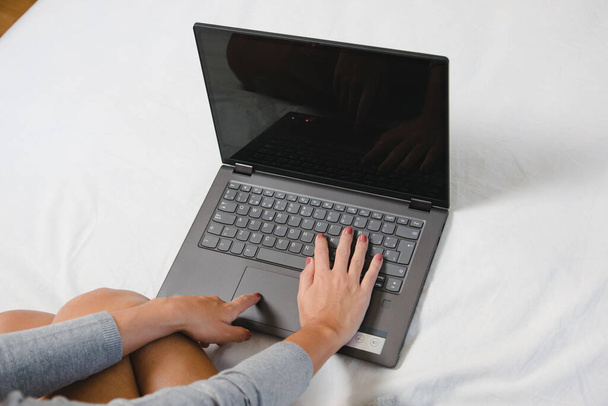 Naisen kädet kirjoittavat kannettavalla tietokoneella kotona etätyön takia virus pandemia. Tyttö mukavassa sängyssä kannettavan tietokoneen avulla - Valokuva, kuva