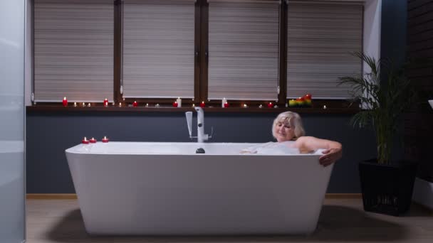 Mooie actieve oudere vrouw ligt in een warm bad met bubbels, genieten van ontspanning. Ouderen - Video