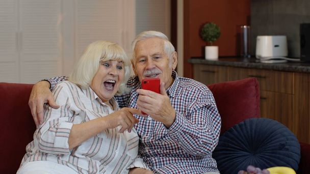 Babička a dědeček dělají videohovory online na mobilním telefonu doma. Usmívající se starší pár - Fotografie, Obrázek