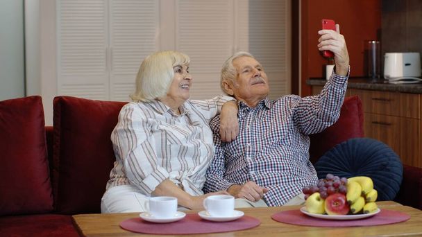 Ηλικιωμένη οικογένεια διασκεδάζει, κάνει selfie φωτογραφίες, εγγραφή βίντεο μαζί στο smartphone στο σπίτι - Φωτογραφία, εικόνα