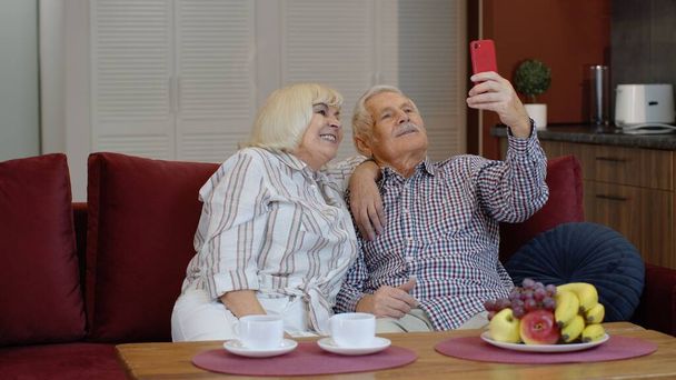 Babcia i dziadek rozmawiają przez internet przez telefon komórkowy w domu. Uśmiechnięta para. - Zdjęcie, obraz