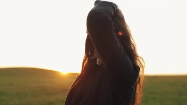 Suloinen nuori nainen suoristaa pitkät hiuksensa auringonlaskua vasten ja lähtee pois selkä käännettynä. Hidastus - Materiaali, video