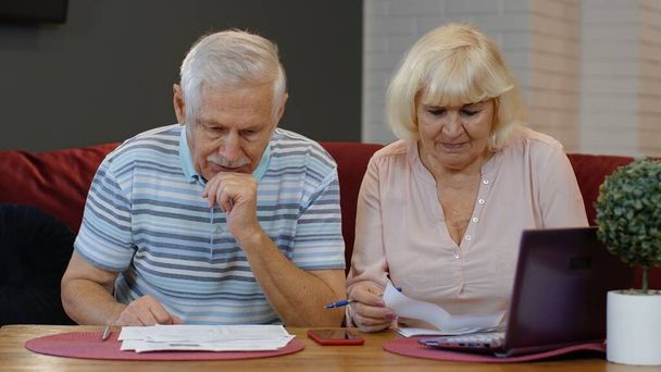 Kıdemli emekli çift ev faturalarını kontrol ediyor ve hesaplıyor. Banka kredisi ödemeleri evrak işlerini yapıyor. - Fotoğraf, Görsel