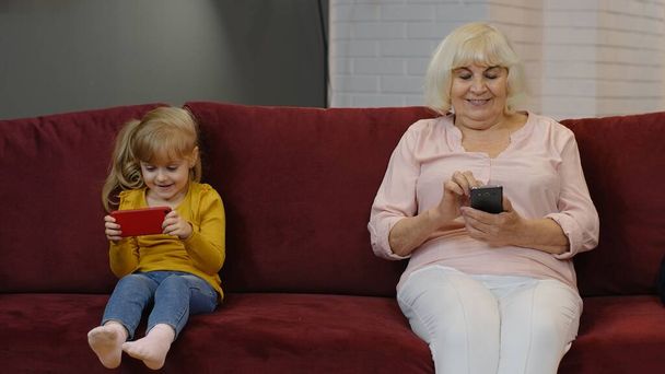 Vanhempi isoäiti, jolla on lapsi tyttö lapsenlapsi, joka käyttää digitaalista matkapuhelinta, pelaa pelejä kotona - Valokuva, kuva