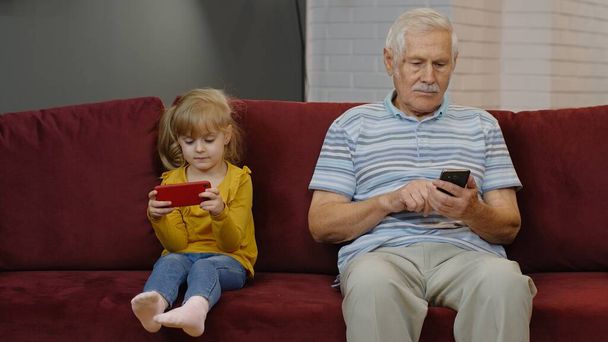 デジタル携帯電話を使用して子供の女の子孫娘とシニア祖父は、自宅でゲームをプレイ - 写真・画像
