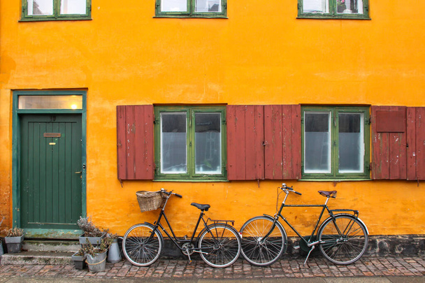 Bicicletas en frente de una fachada de casa de color naranja amarillo en Nyboder, histórico distrito de la casa fila de antiguos cuarteles navales en Copenhague, Dinamarca. Pintoresca ciudad europea de jalá. Royal Danish Navy - Foto, Imagen