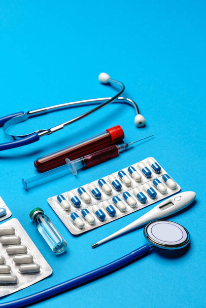 Stethoscope, syringe, test tubes with blood samles and ampoules with medicine or vaccine over blue background - Foto, afbeelding