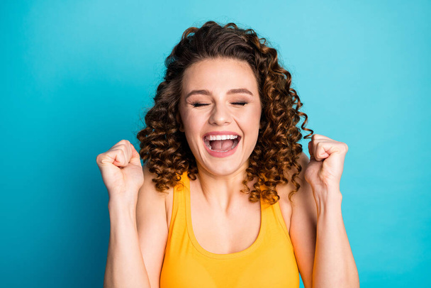 Photo of funny redhead young girl raise fists close eyes open mouth excited wear yellow tank-top isolated blue color background - 写真・画像