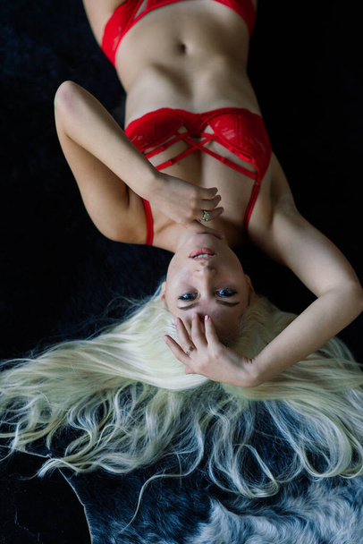 Modella sexy con capelli biondi, posa in camera da letto di lusso, indossando lingerie rossa, soft focus - Foto, immagini