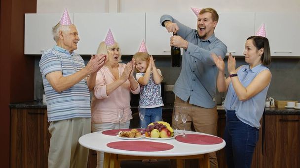 Члены многодетной семьи с ребенком-девочкой празднуют день рождения. Открытие шампанского - Фото, изображение