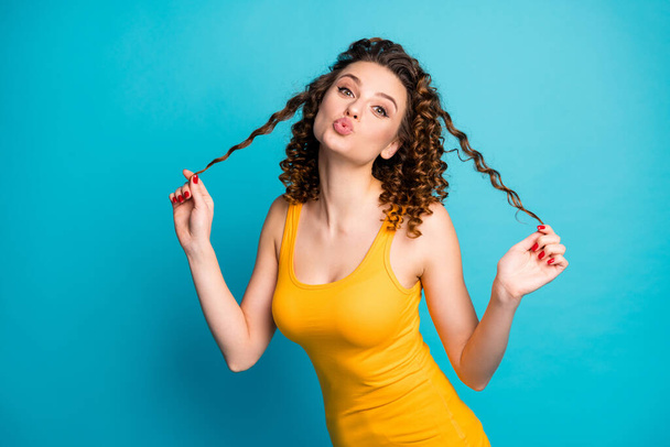 Photo of cute charming girl romantic look playing curls send air kiss wear yellow tank-top isolated blue color background - 写真・画像