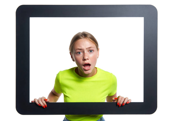 Indignant girl peeking through digital tablet frame over white background - Foto, imagen