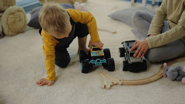 Grappige jongen die met een speelgoedtruck op de vloer speelt. Broers en zussen brengen tijd door in huis - Foto, afbeelding