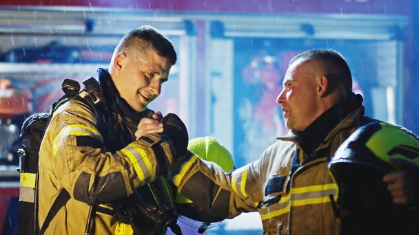 Портрет двух молодых пожарных на дожде перед пожарной машиной в полной форме. Огненный дриль - Фото, изображение