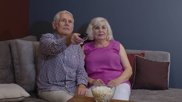 Senior viejo pareja sosteniendo control remoto hablando riendo viendo humor tv show sentado en sofá - Foto, Imagen