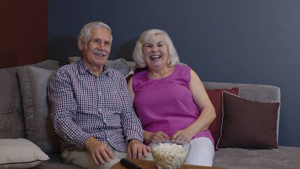 Portrait de couple âgé regardant la télévision à la maison manger du pop-corn profiter du film ensemble à la maison - Photo, image
