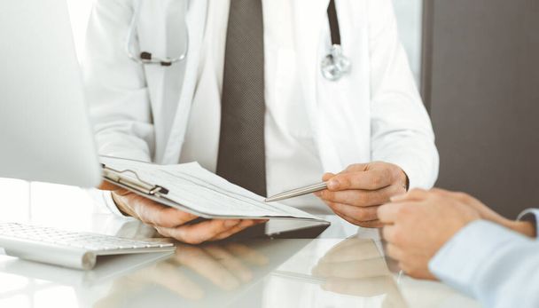 Unknown male doctor and woman-patient discussing current health examination while sitting in clinic and using clipboard. Good medical service in hospital. Medicine concept - Photo, Image