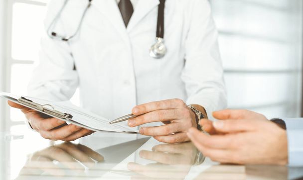Unknown male doctor and woman-patient discussing current health examination while sitting in clinic and using clipboard. Good medical service in hospital. Medicine concept - Photo, Image