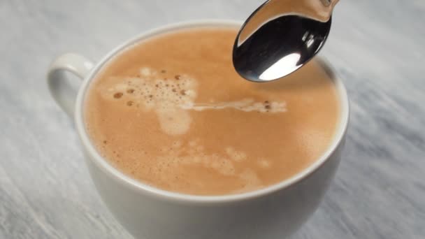 Person hand stirring coffee with spoon in white cup on gray textured wooden table. Close-up - Video