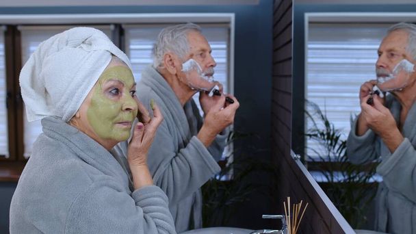 Senior γιαγιά εφαρμογή μάσκα προσώπου και ο παππούς ξύρισμα με το χέρι λεπίδα ξυράφι στο μπάνιο - Φωτογραφία, εικόνα