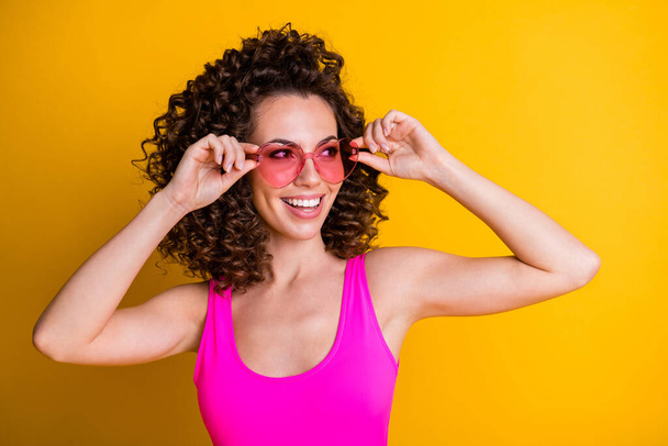Closeup photo of attractive cute girlish wavy hairdo lady enjoy summer traveling holidays try on new cool youth sun specs heart shape wear pink tank top isolated yellow color background - Fotografie, Obrázek