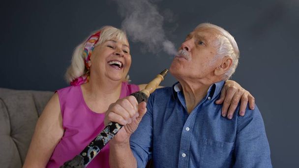 Pareja mayor fumando narguile en casa. Abuela y abuelo mayores divertirse, relajarse - Foto, imagen