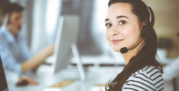 Business woman using headset for communication and consulting people at customer service office. Call center. Group of operators at work at the background. Casual dress style - Fotografie, Obrázek
