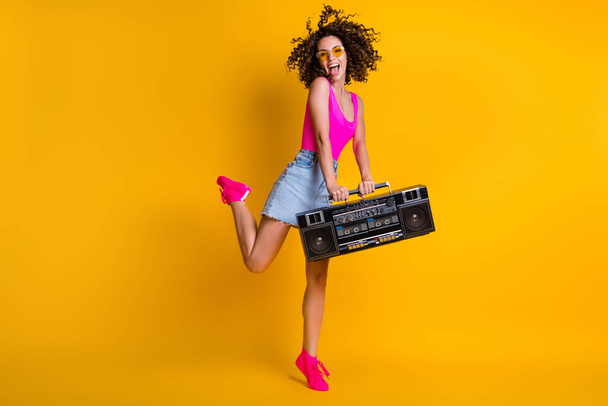 Full size photo of attractive lady hold retro boom box recorder chill students event holiday rejoice enjoy music wear sun specs pink singlet denim skirt shoes isolated yellow color background - 写真・画像