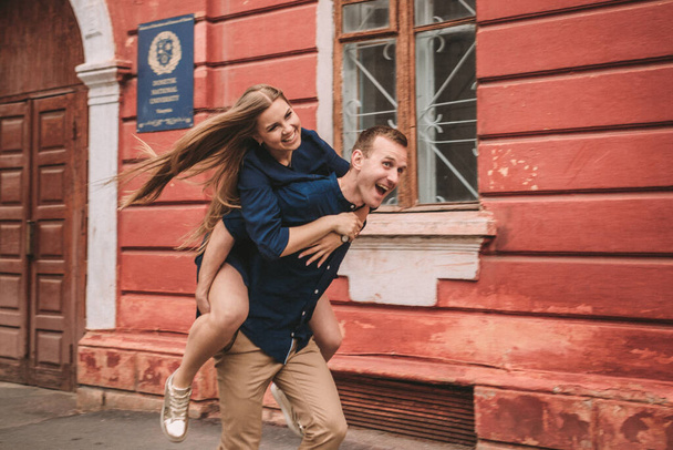 L'état heureux d'un jeune couple sur fond de mur rouge, la fille a sauté sur le gars - Photo, image