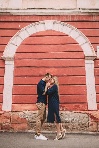 Jong stel verliefd op de achtergrond van een rode muur. Gelukkig getrouwd stel op een wandeling in de stad - Foto, afbeelding