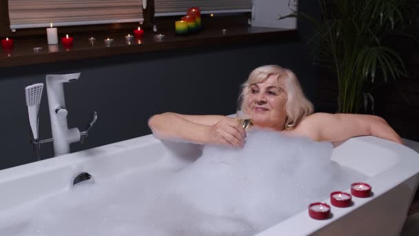 Seniorka babička si dává pěnovou koupel, pije šampaňské v luxusní koupelně se svíčkami - Záběry, video