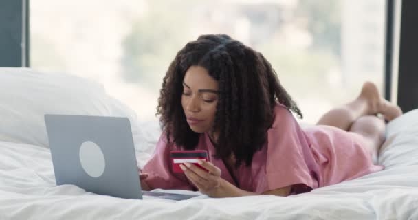 Fiatal afro-amerikai hölgy online vásárlás fekvő ágyban laptoppal és hitelkártyával - Felvétel, videó