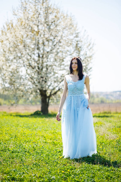 Açık mavi elbiseli bir kızın portresi. Saçında çiçek açan bir ağaca karşı süslenmiş.. - Fotoğraf, Görsel