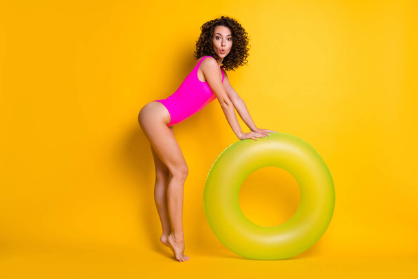Full length profile photo of charming amazed curious lady relax rest resort hold hands big green round circle swimming pool sea ocean wear pink swimsuit isolated vivid yellow color background - Photo, Image