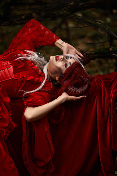 Maleficent Woman in Red Clothing and Horns in dark Forest. Posing in magik forest - Foto, Bild