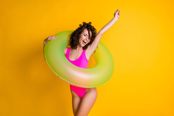 Photo portrait of young woman in pink swim wear holding green inflatable ring cheering for victory dancing isolated on vivid yellow colored background - Zdjęcie, obraz