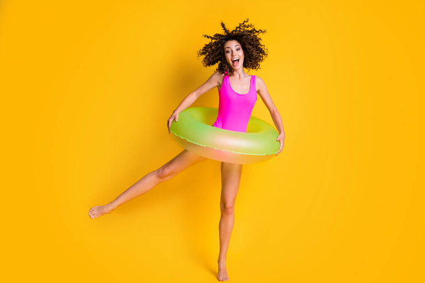Photo portrait of excited woman standing on one leg holding green inflatable circle with two hands screaming wearing pink swim wear isolated on vivid yellow colored background - Foto, Imagem