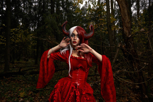 Зловісна жінка у червоному одязі та рогах у темному лісі. Посадка в лісі. - Фото, зображення